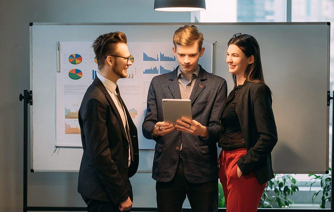 Three people are standing in a room looking at an ipad.