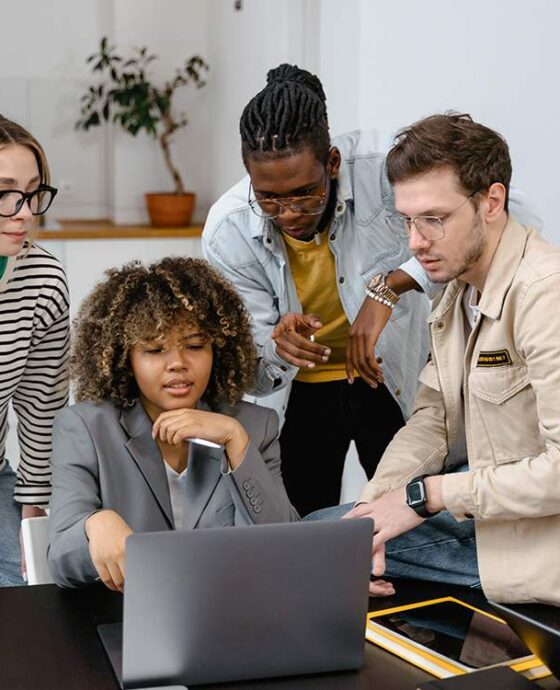 A group of people sitting around a table looking at a laptop.