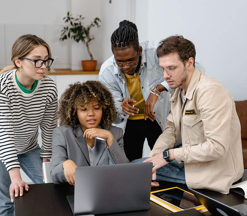 A group of people sitting around a table looking at a laptop.