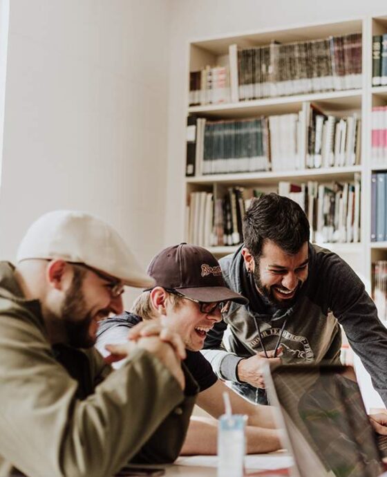 Three men are looking at a laptop in front of them.