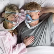 A man and woman laying in bed with cpap masks on.