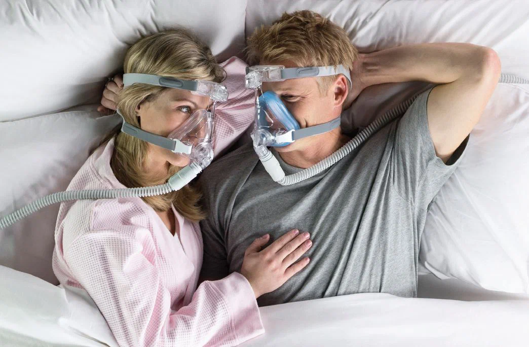 A man and woman laying in bed with cpap masks on.