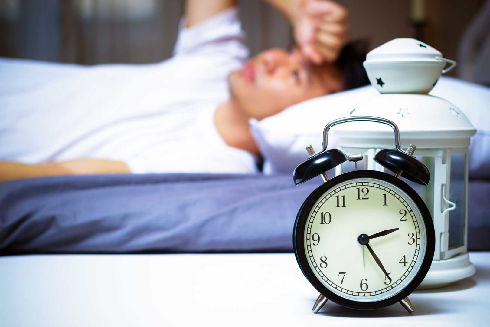 A person laying in bed with an alarm clock.