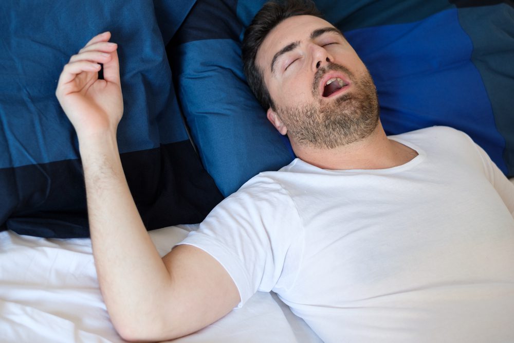 A man is laying in bed with his mouth open.