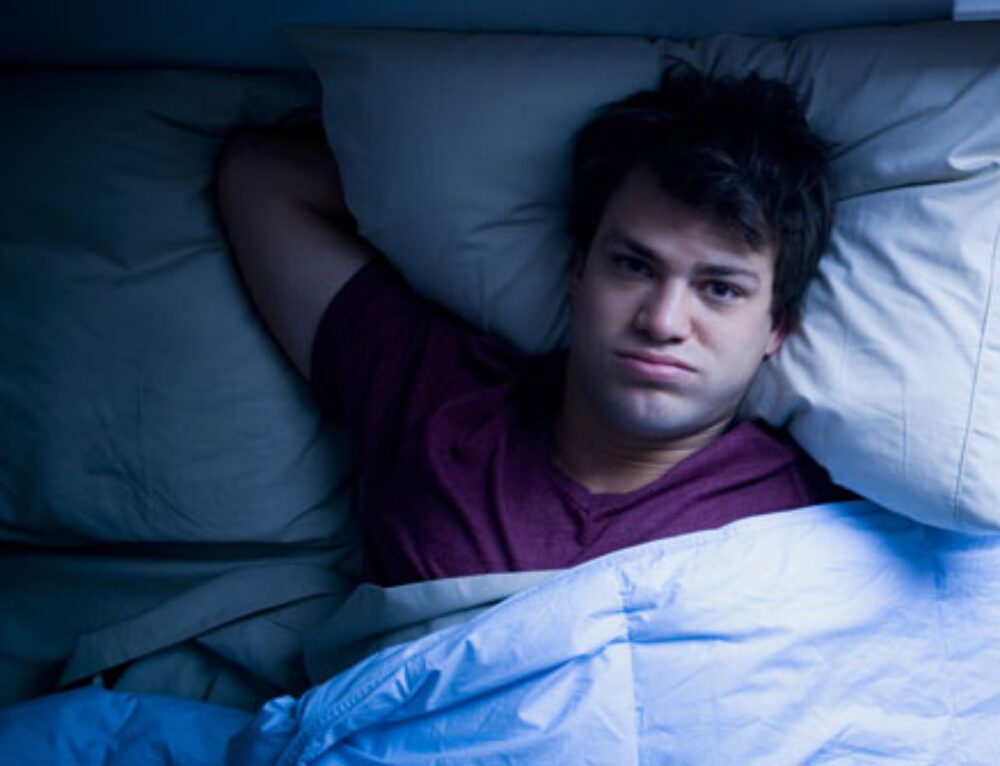 A man laying in bed under the covers.